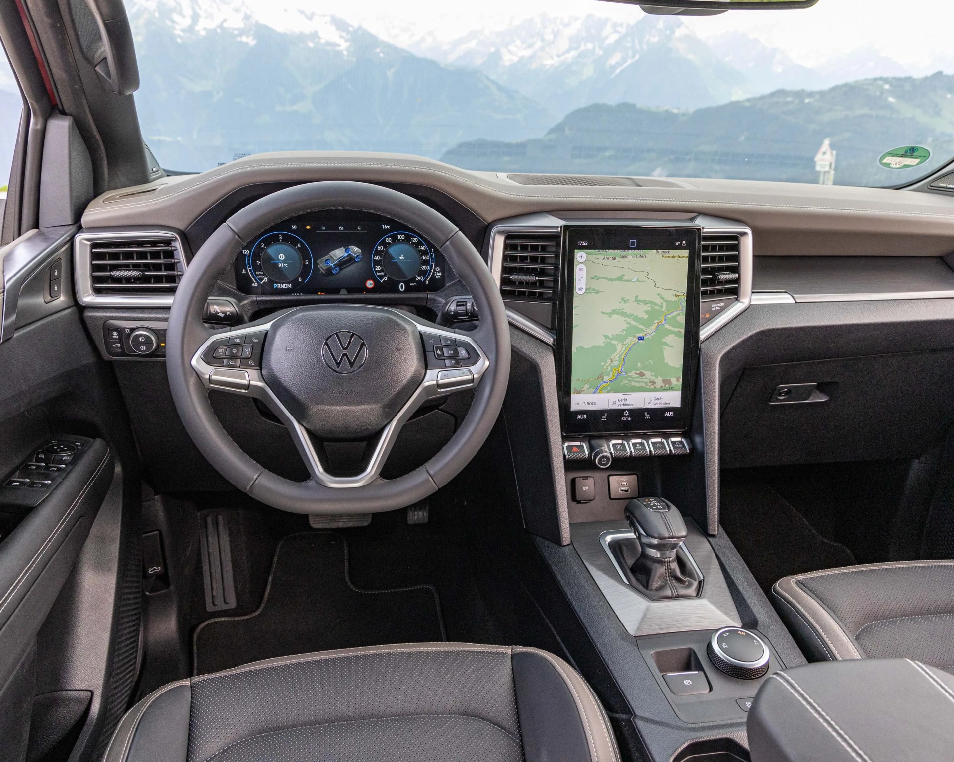 Black leather Volkswagen steering wheel and dashboard with digital display and vertical touchscreen in a car interior.