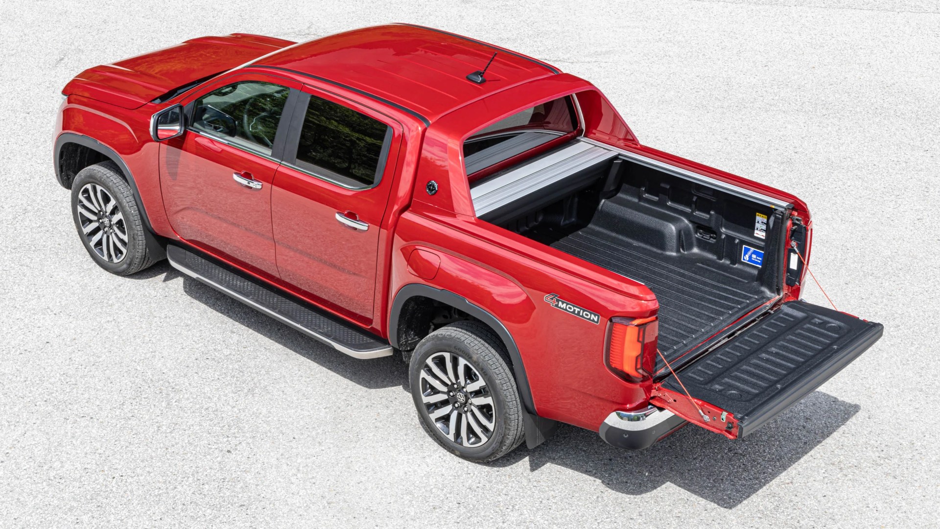 Red Volkswagen pickup truck with open tailgate and black bed liner, viewed from above on a light pavement.