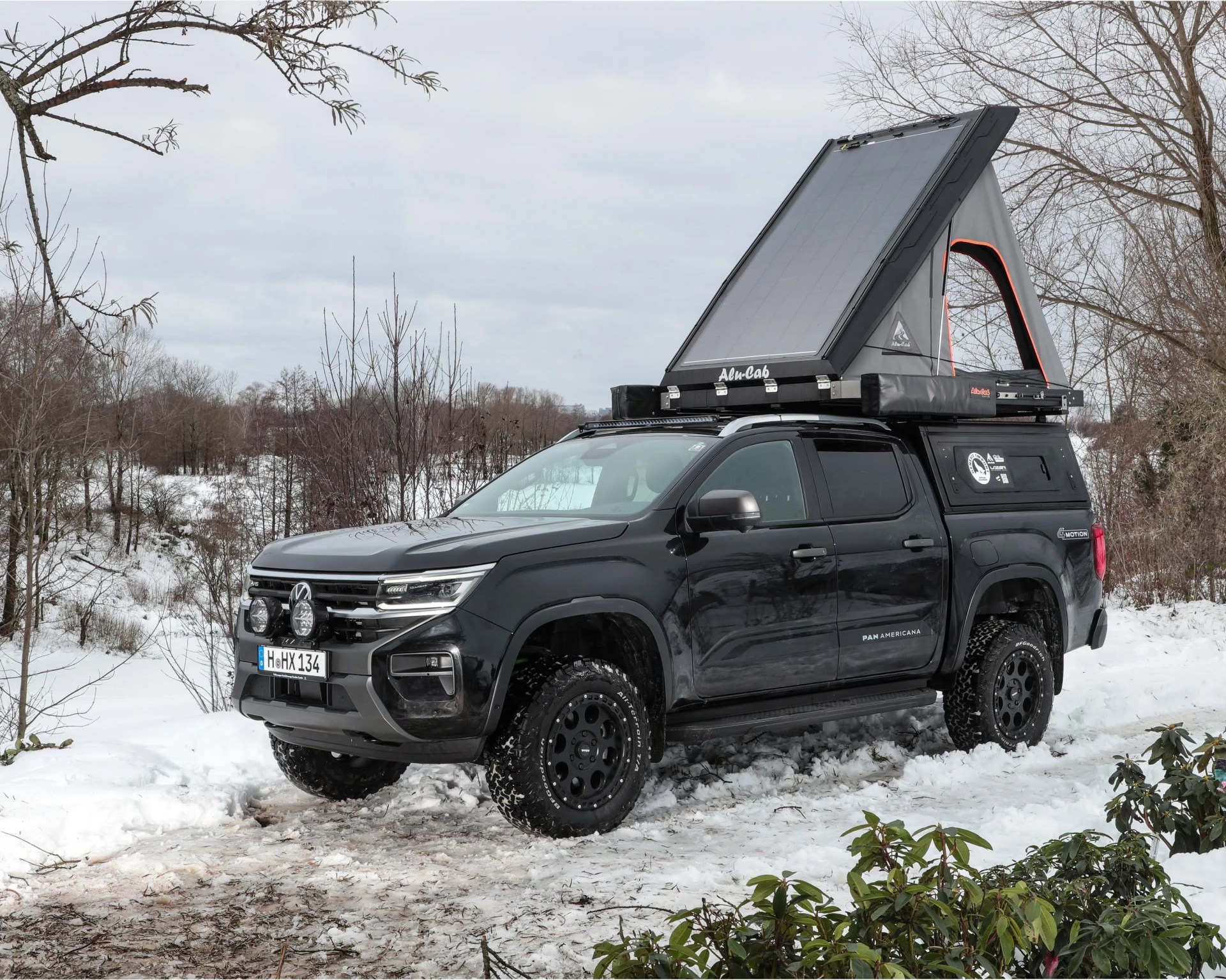 Black Volkswagen Amarok Panamericana pickup truck with rooftop tent in snowy forest.