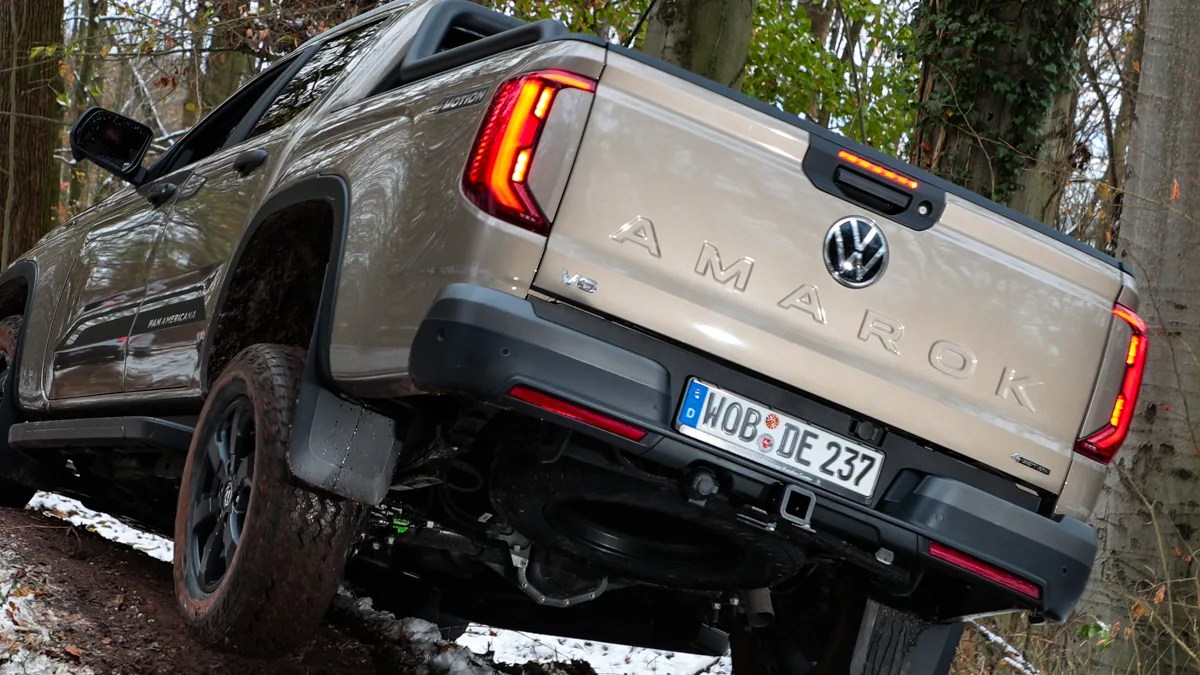 Beige Volkswagen Amarok V6 pickup truck with black trim and off-road tires on a muddy forest trail.
