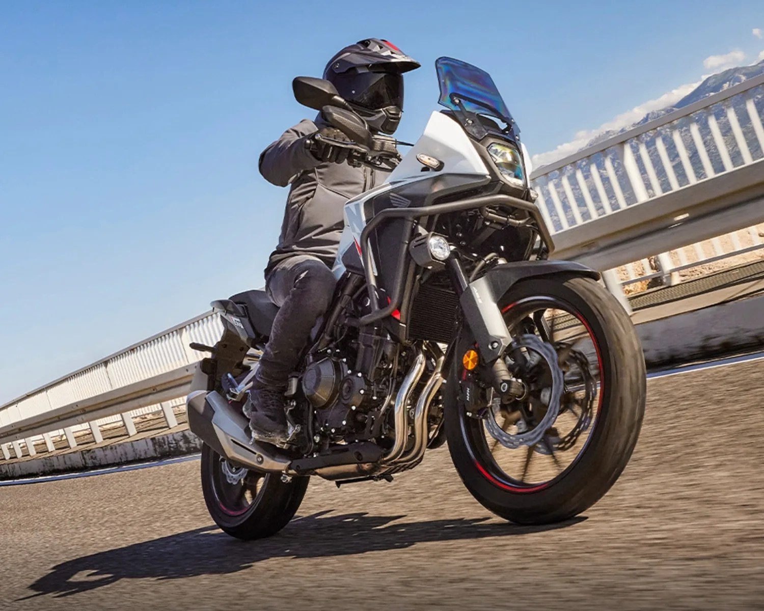 Person riding a white and black adventure motorcycle with a tinted windshield on a paved road.