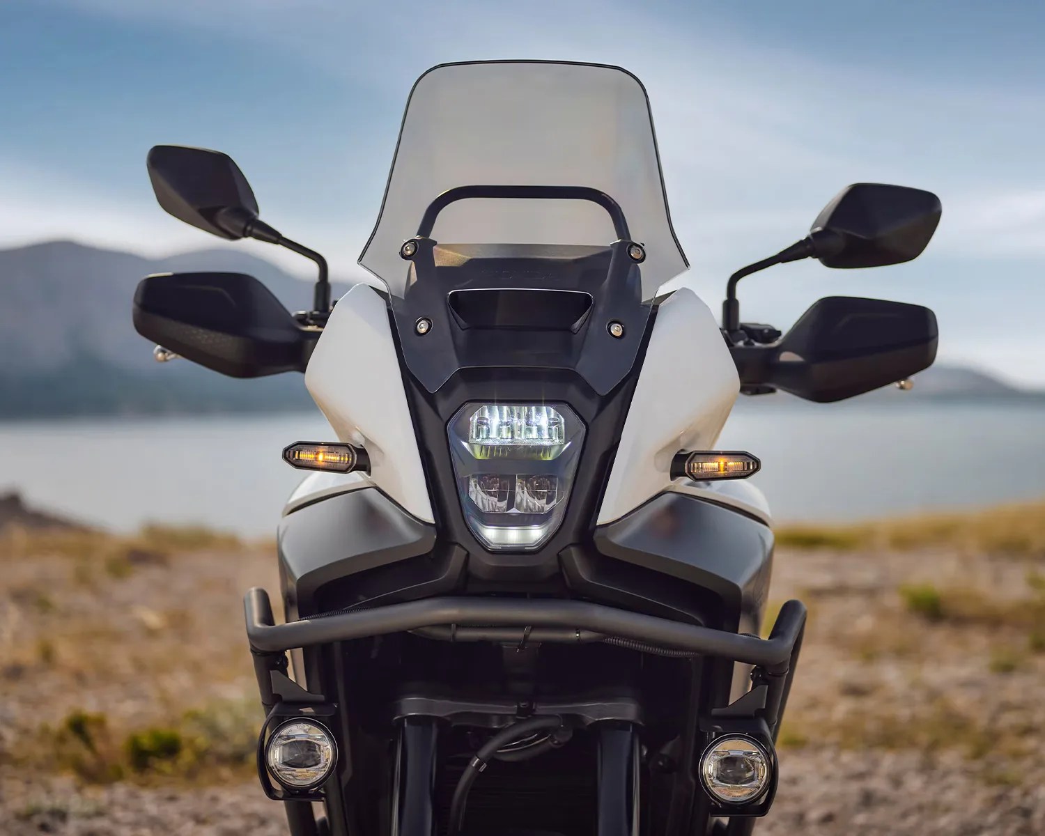 Front view of a white and black adventure motorcycle with a tall windshield and dual round auxiliary lights.