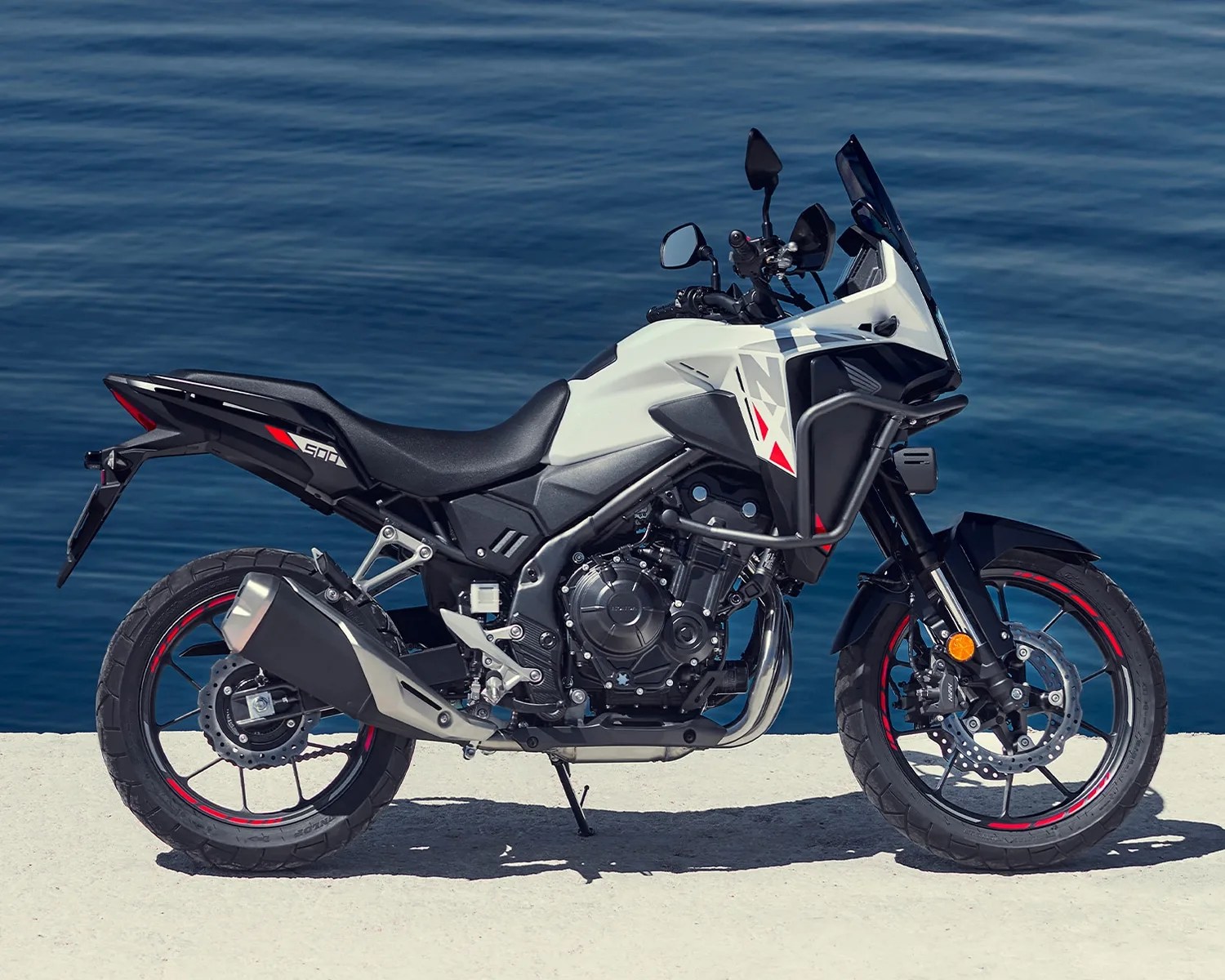 White and black Honda NX 500 motorcycle with red accents parked on a concrete surface by the water.