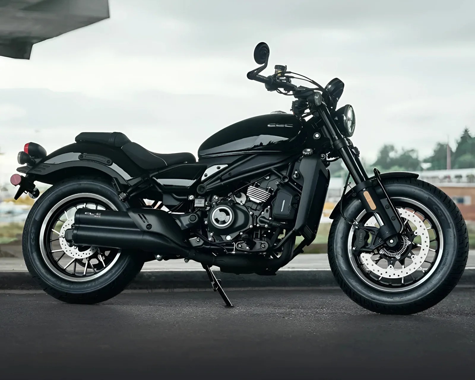 Black cruiser motorcycle with dual exhaust pipes parked on asphalt under an overhang.