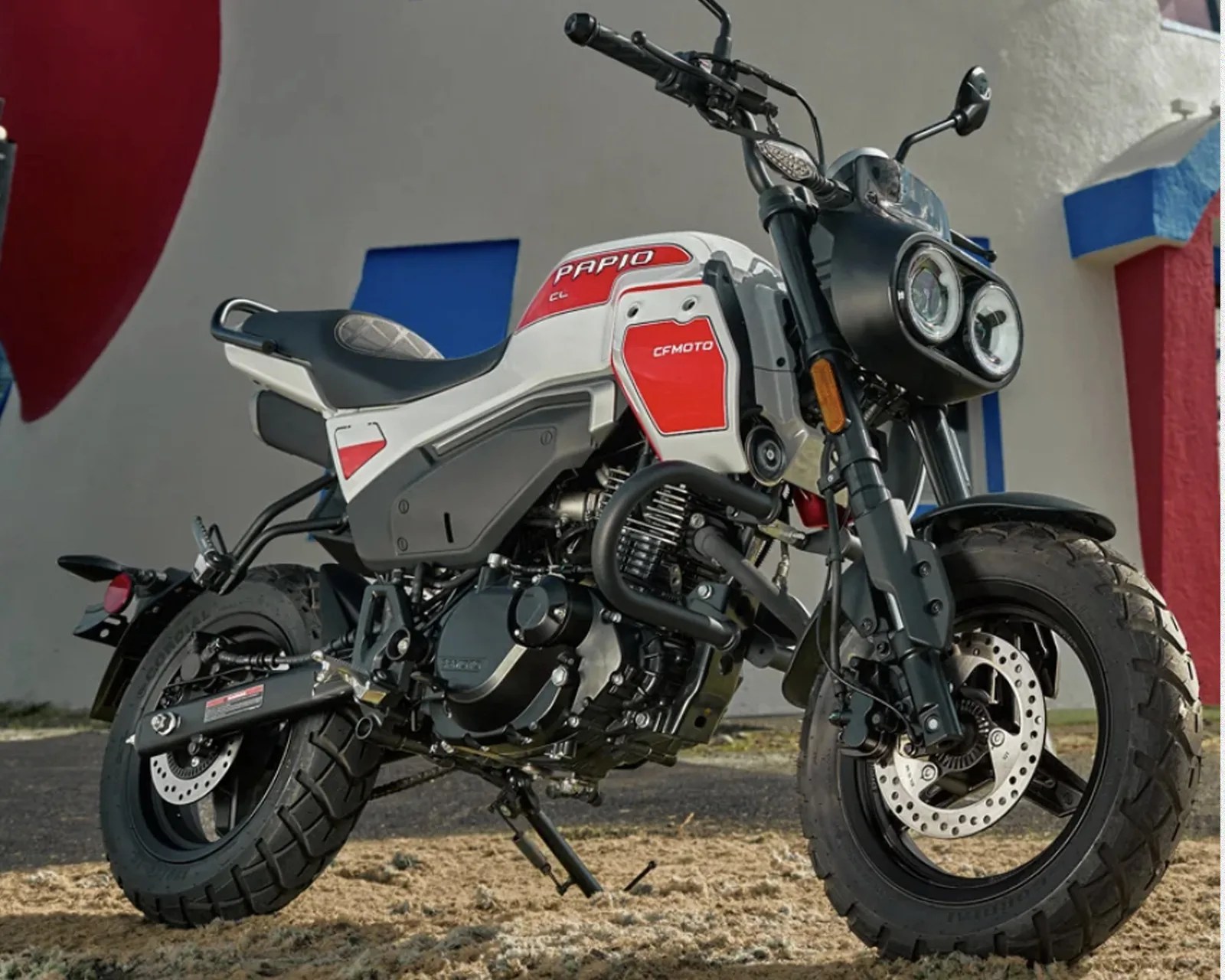 White and red CFMOTO Papio motorcycle with dual round headlights parked on grass.