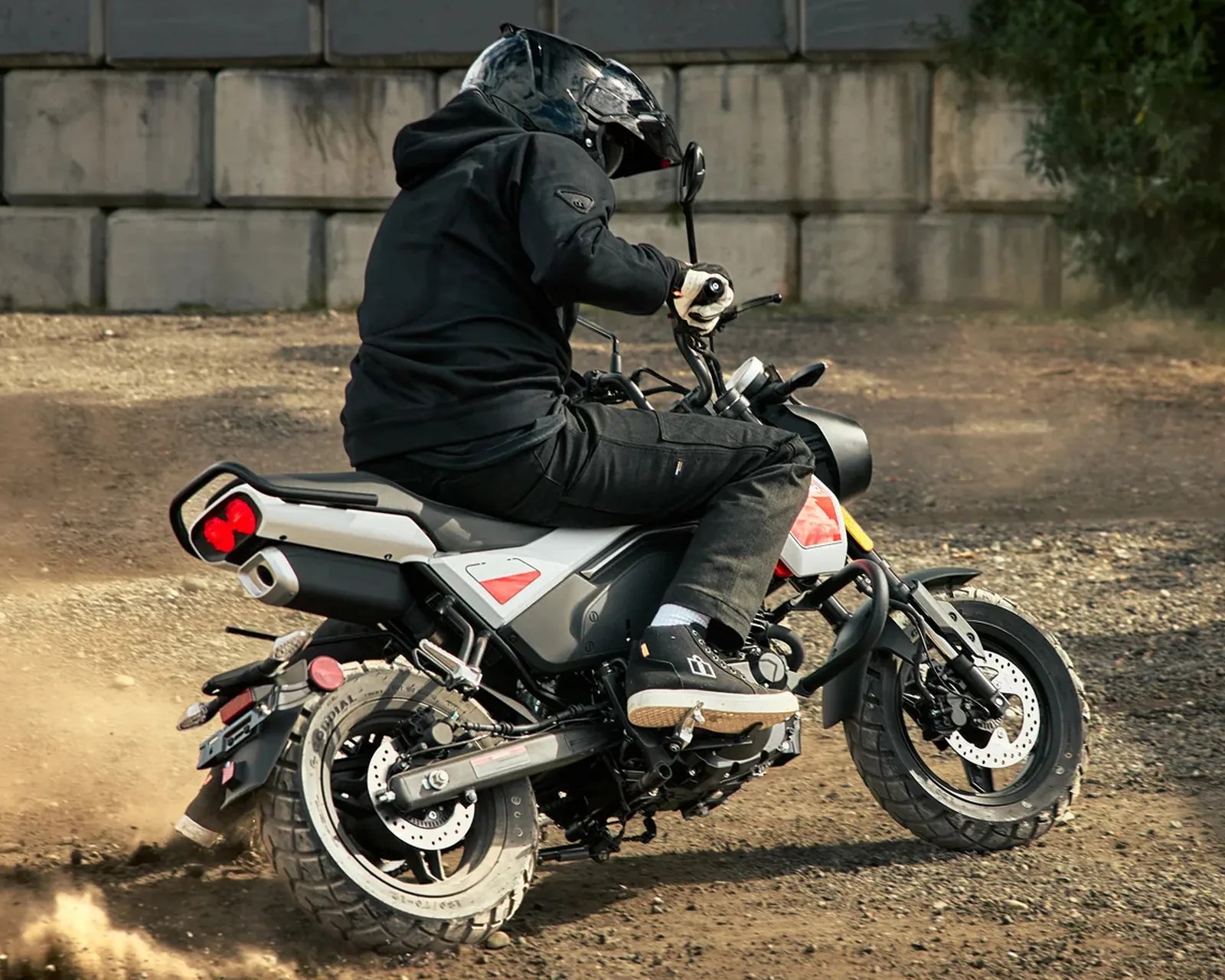 Person wearing black helmet and jacket riding a white and black motorcycle on a dirt surface.