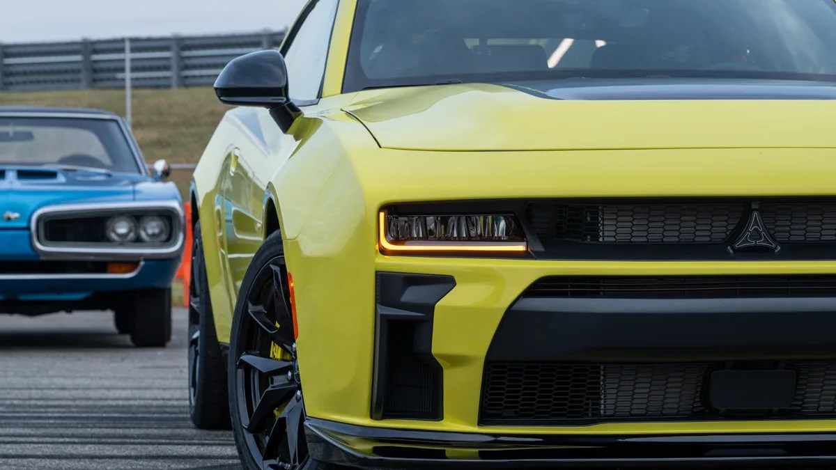 Front view of a yellow sports car with black grille and headlights, with a blue vintage car in the background.