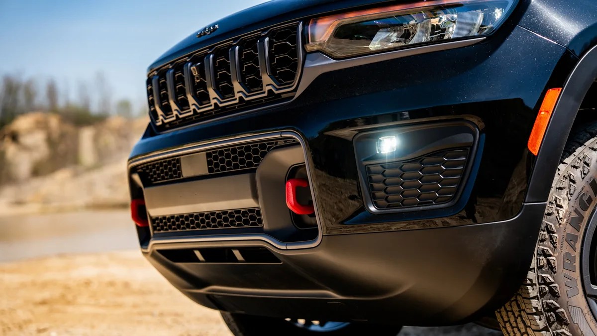 Front close-up of a black Jeep SUV showing the grille, headlight, red tow hook, and rugged tire.