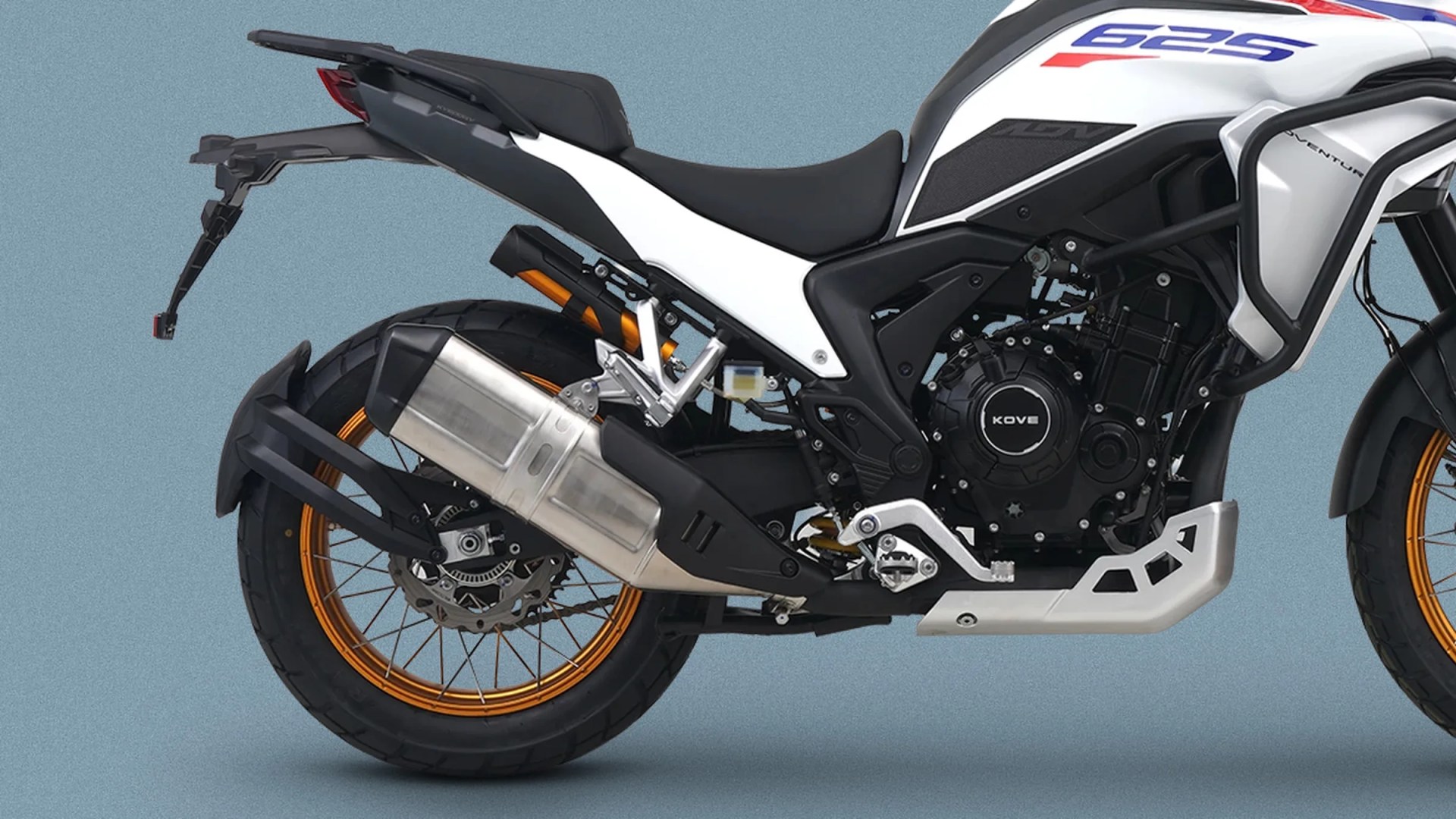 White and black adventure motorcycle with orange spoked wheels and large silver exhaust on a blue background.