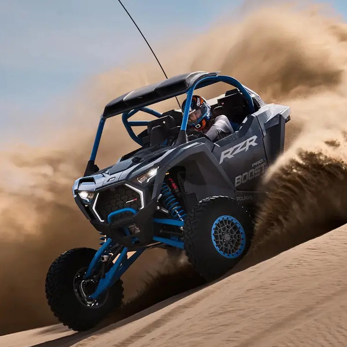 Black and blue Polaris RZR off-road vehicle kicking up sand on a dune with a driver wearing a helmet.