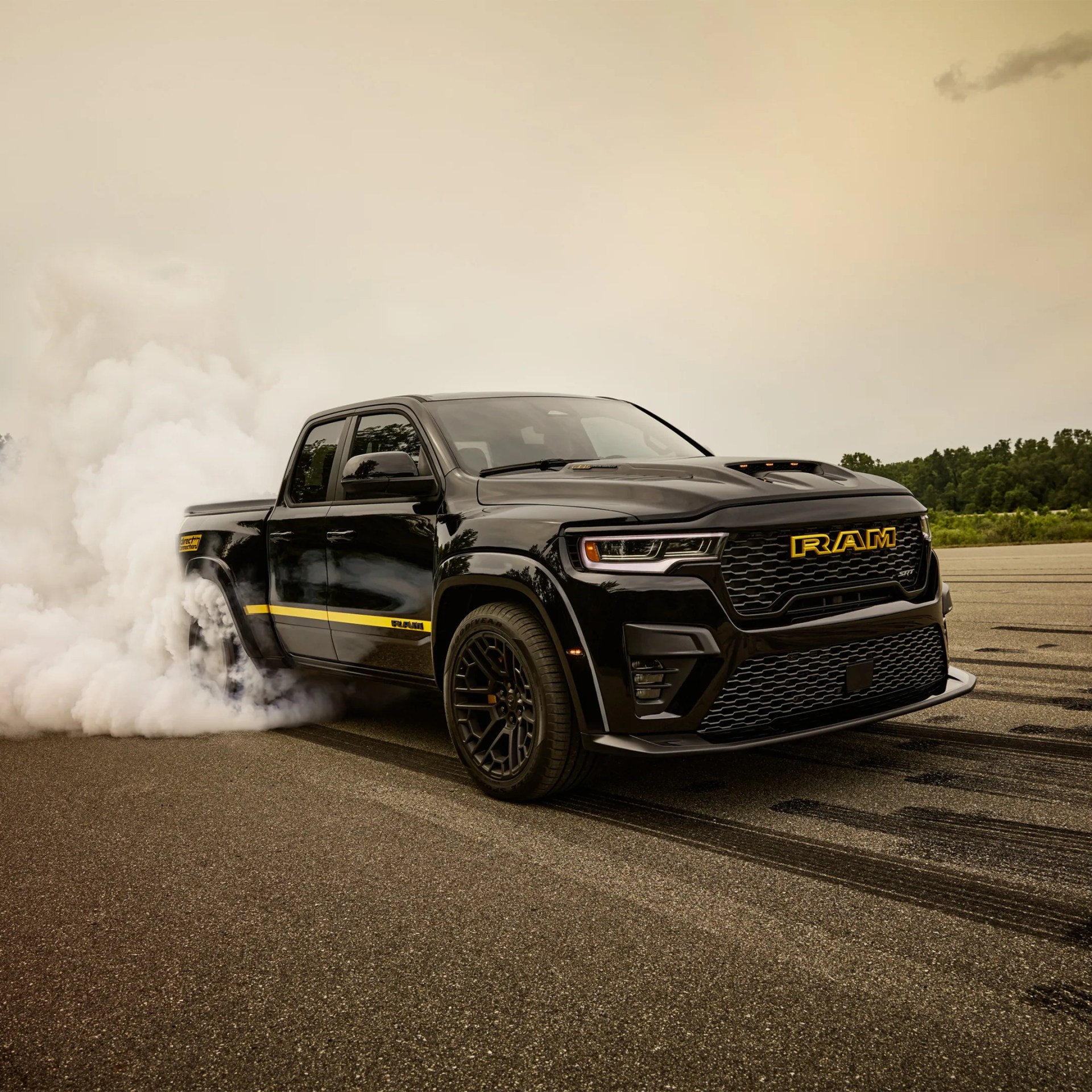 Black RAM SRT pickup truck with yellow accents performing a burnout on asphalt with smoke around rear tires.