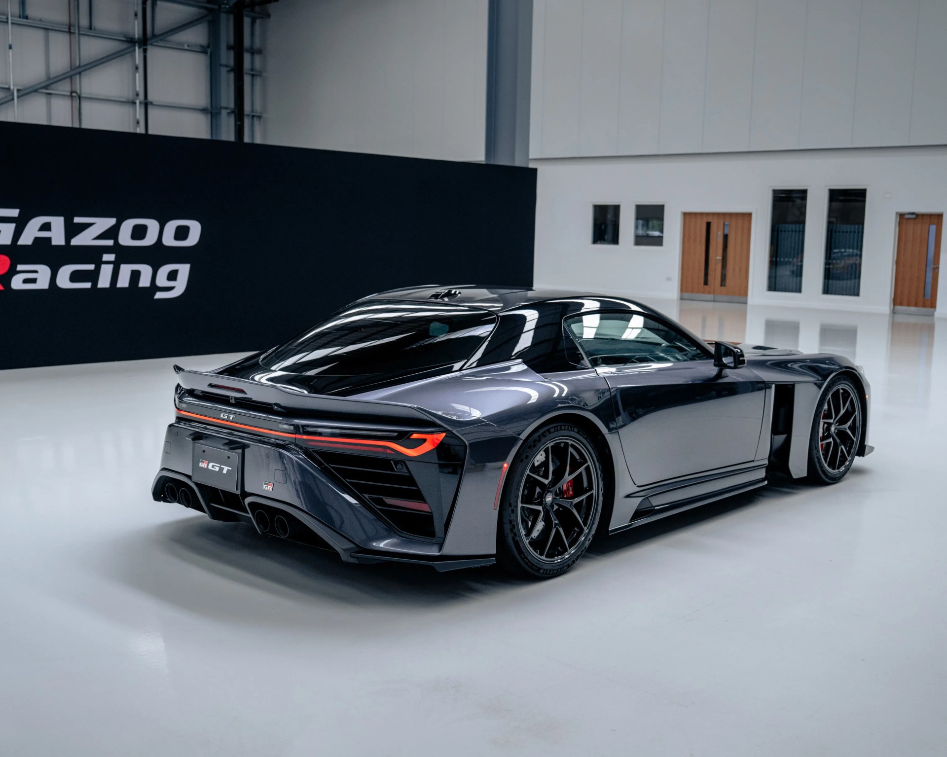 Glossy black Toyota GR GT sports car rear and side view inside a showroom with Gazoo Racing sign in background.