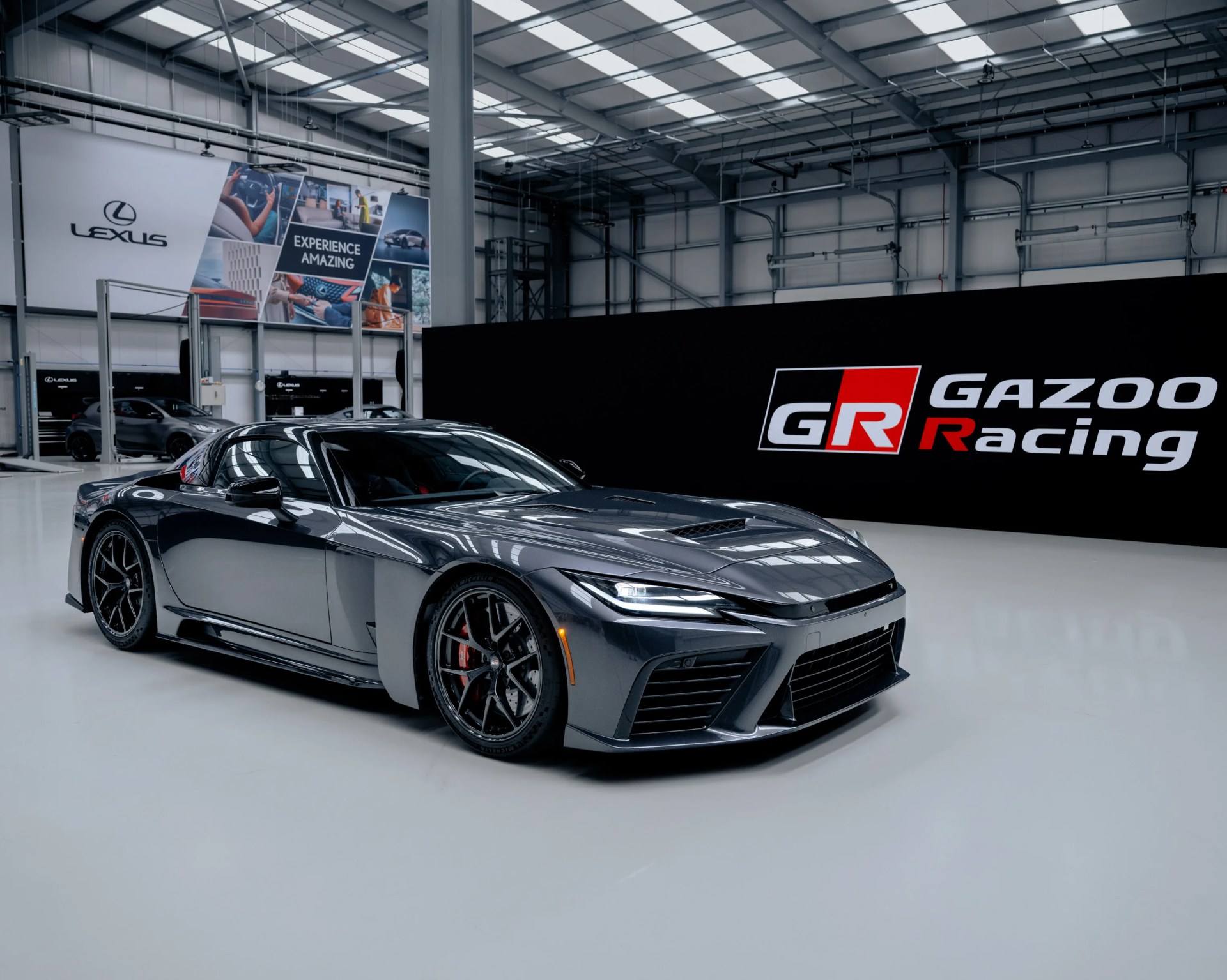 Glossy dark gray Lexus sports car with black wheels in a bright showroom with Lexus and Gazoo Racing logos.