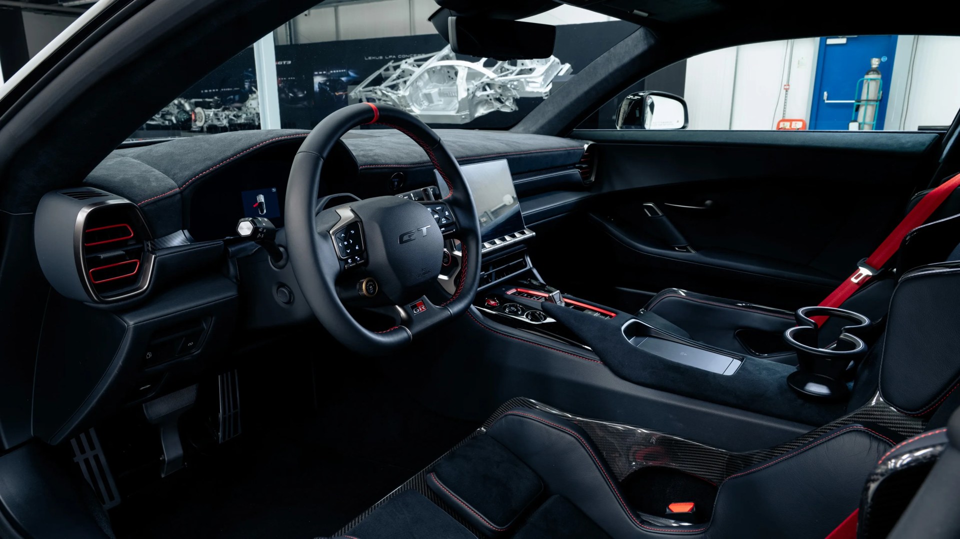 Black sports car interior with red stitching, carbon fiber accents, digital display, and red seatbelt.