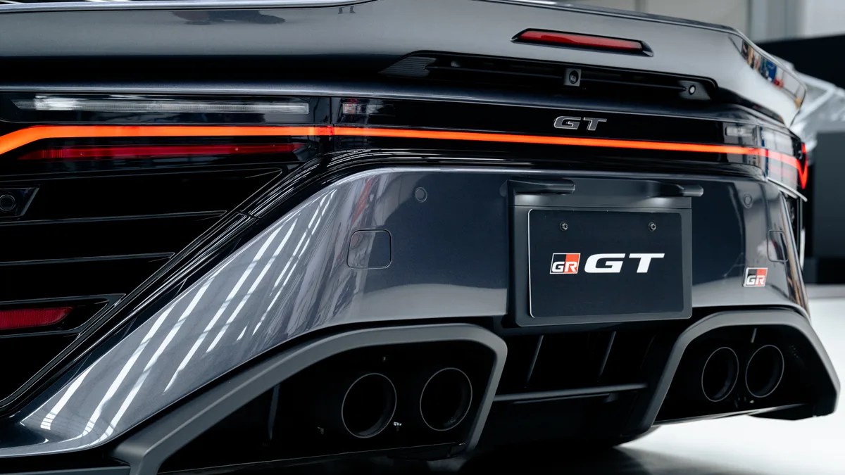 Rear close-up of a black GR GT car showing quad exhaust pipes and illuminated taillights.