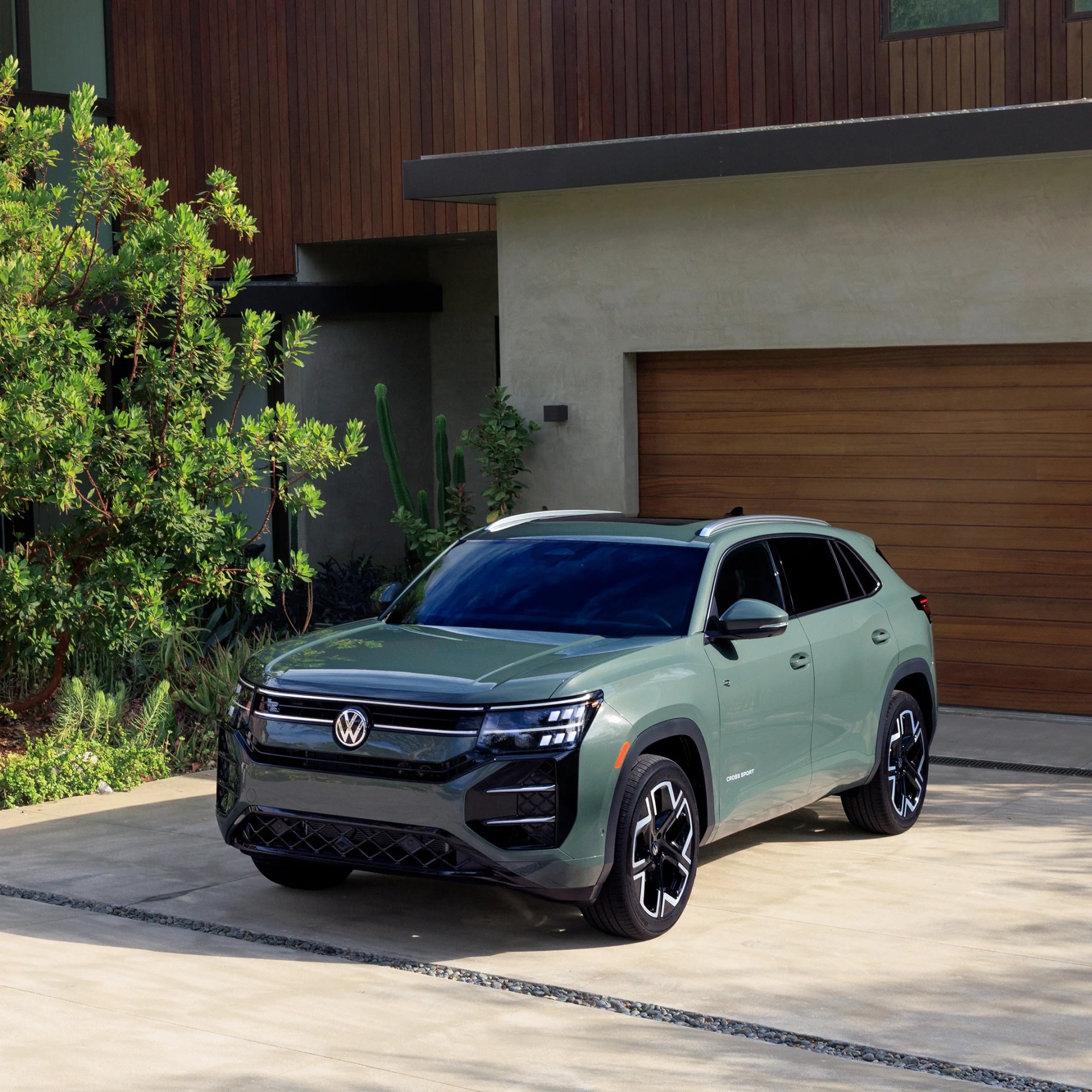 Green Volkswagen SUV parked in front of a modern house with wooden garage door and greenery.