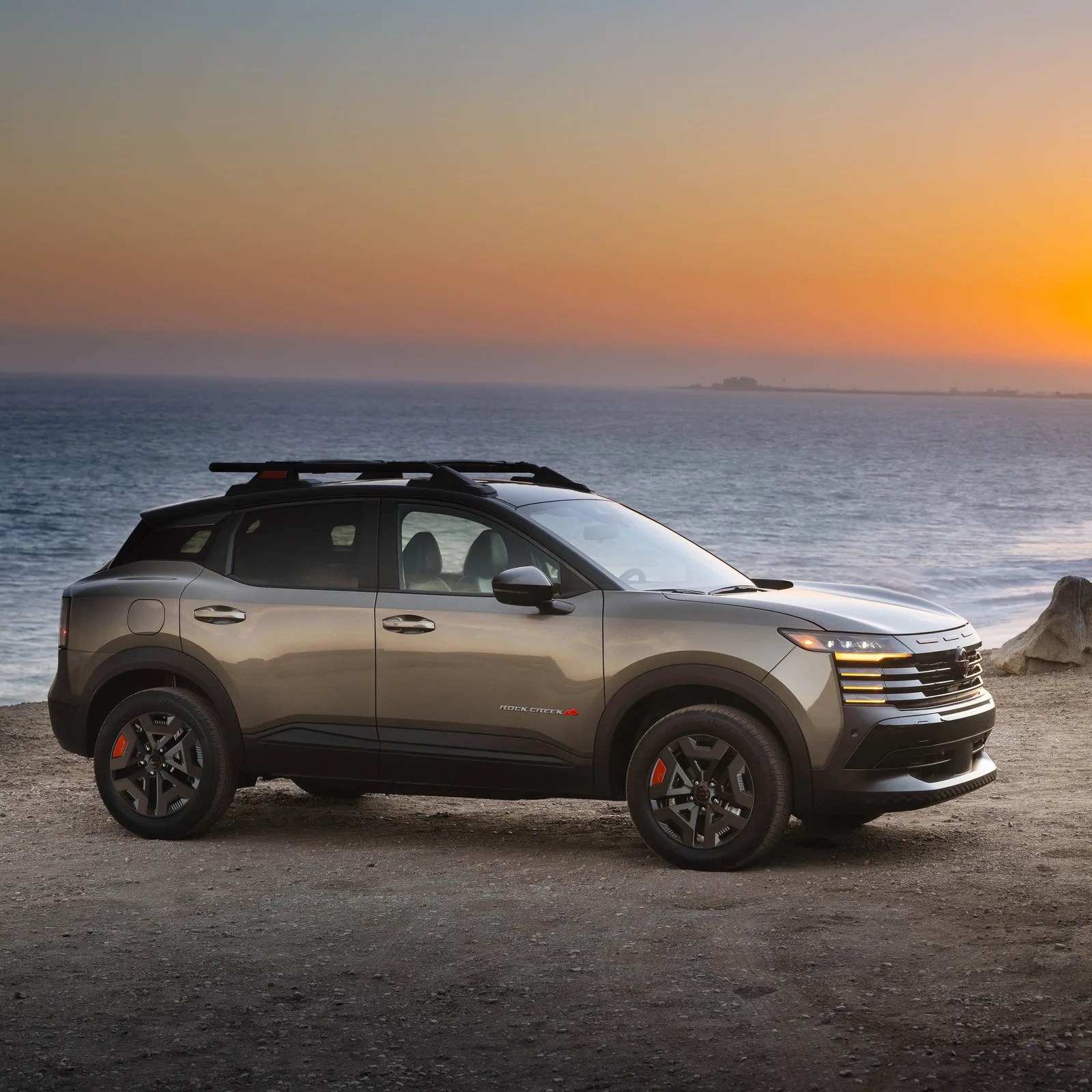 Metallic gray SUV with black roof rails parked on a beach at sunset.