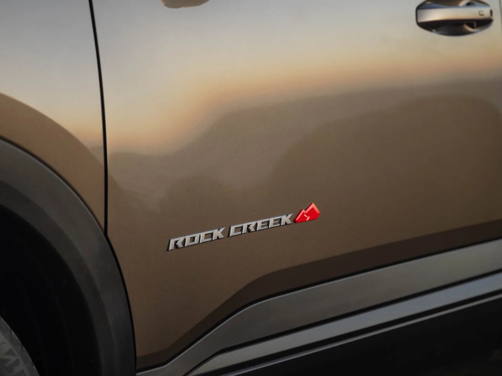 Close-up of a brown car door with a silver "ROCK CREEK" badge and a red mountain logo near the bottom.