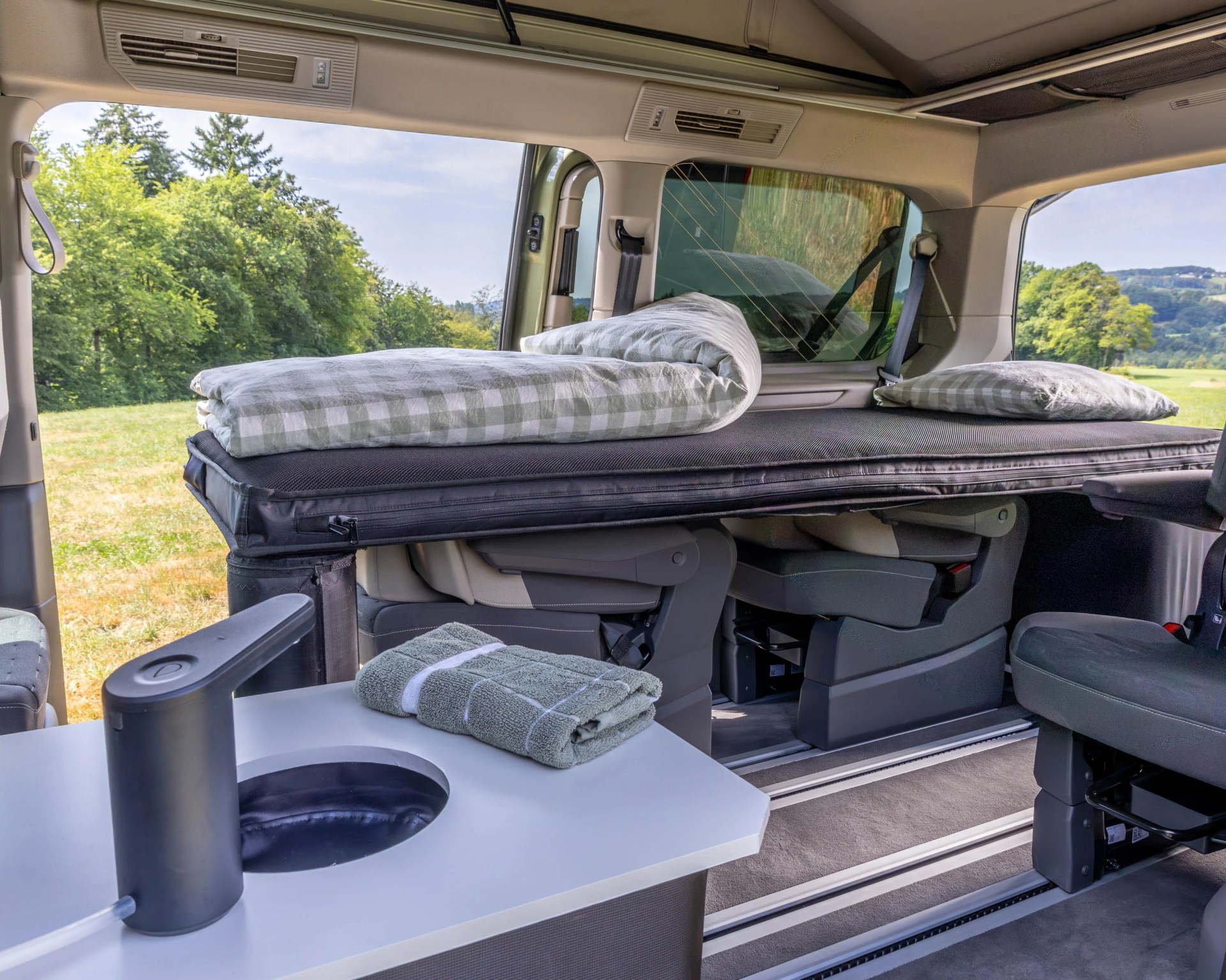 Folded green towels on a white table inside a camper van with a folded bed and pillows in the background.