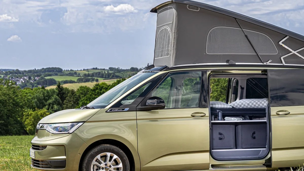 Gold Volkswagen camper van with pop-up roof and open sliding door showing interior bed and storage bins.
