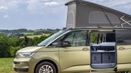 Gold Volkswagen camper van with pop-up roof and open sliding door showing interior bed and storage bins.