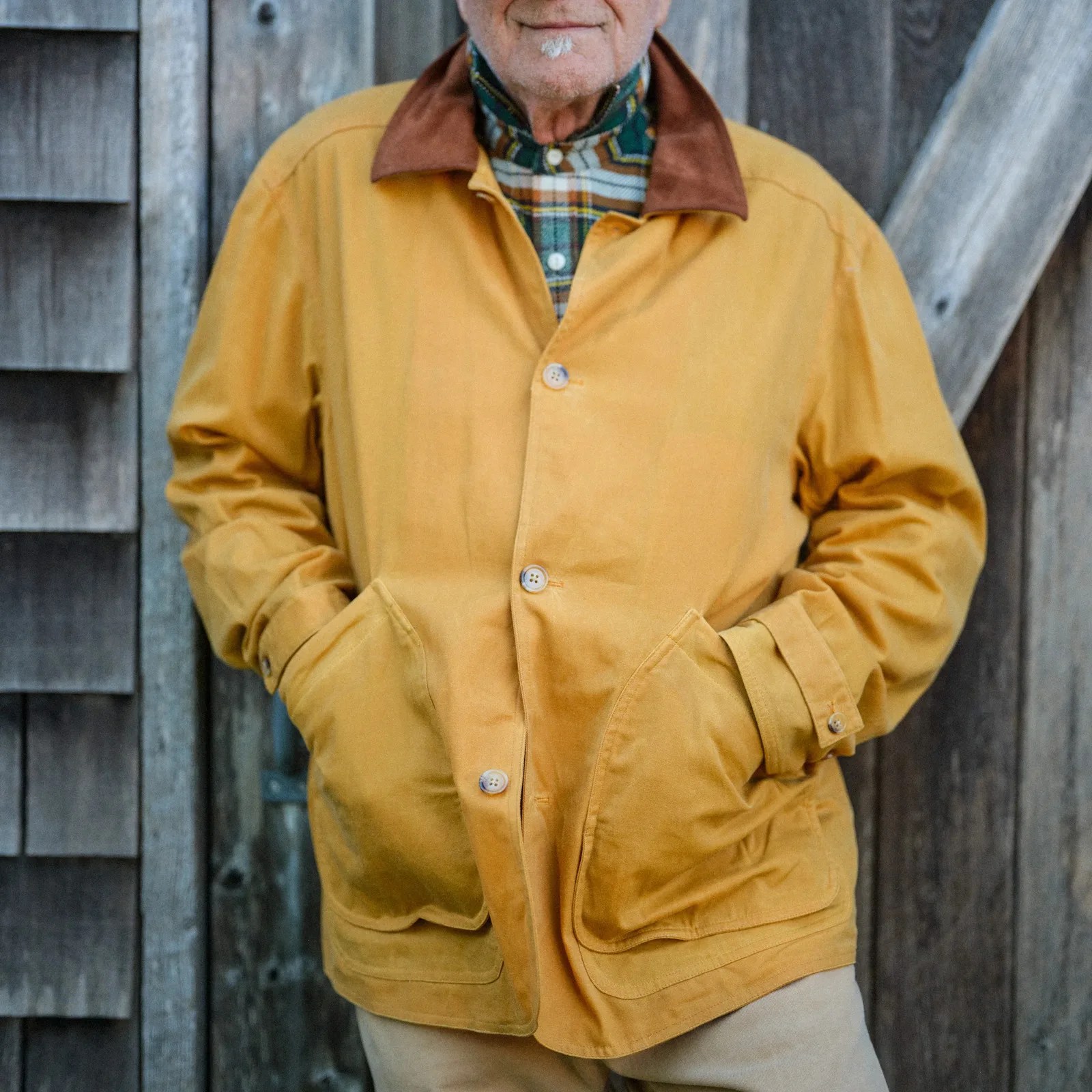 Mustard yellow jacket with brown collar and large front pockets worn over a plaid shirt.