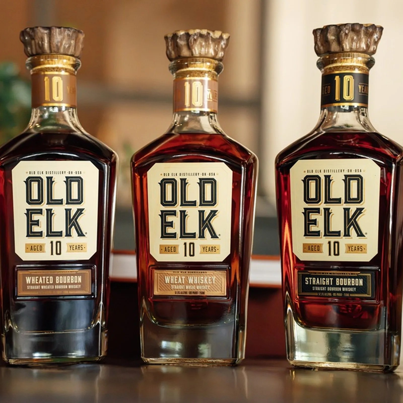 Three bottles of Old Elk 10-year aged whiskey, labeled Wheated Bourbon, Wheat Whiskey, and Straight Bourbon.
