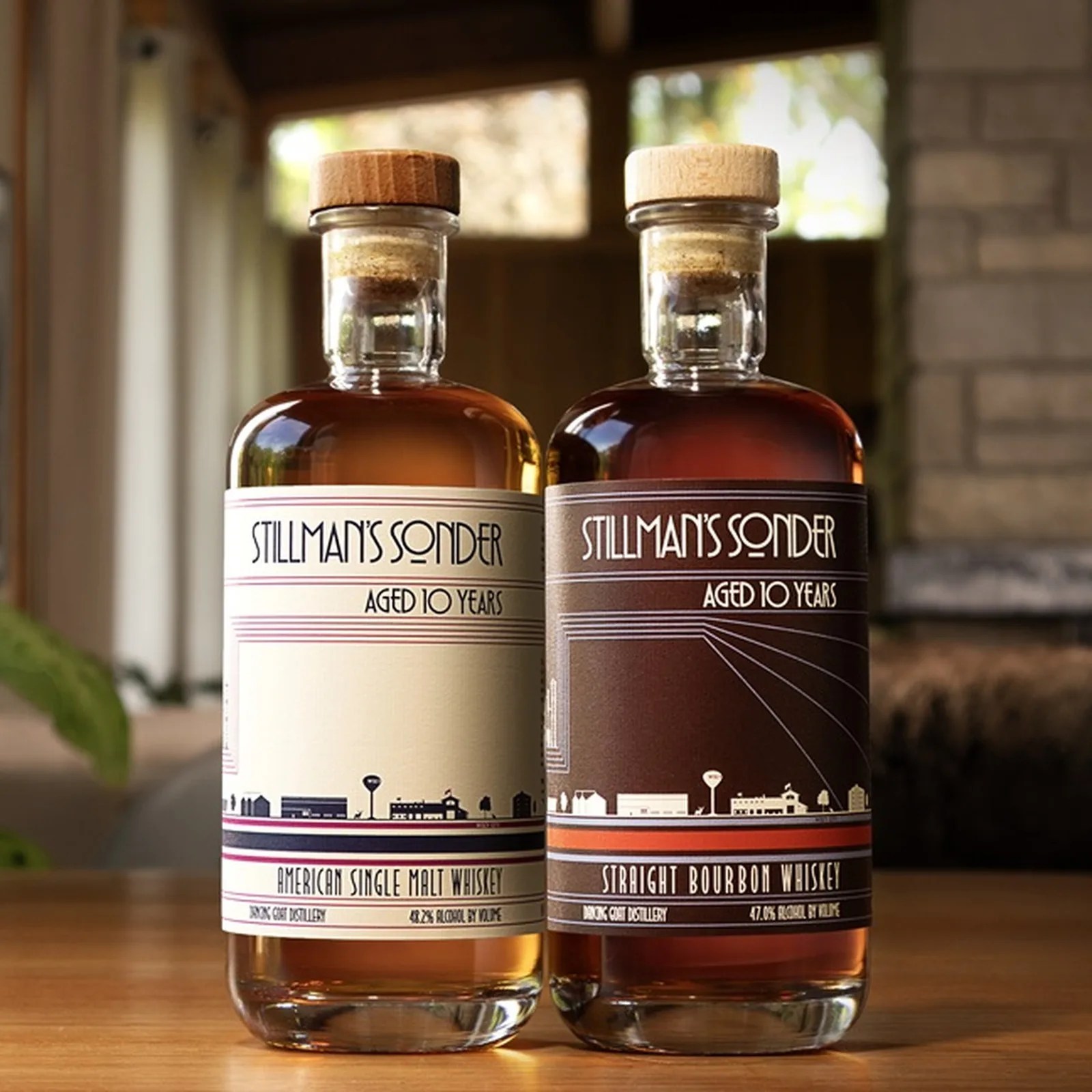 Two Stillman's Sonder whiskey bottles with wooden corks, one labeled American Single Malt and the other Straight Bourbon, on a wooden surface.