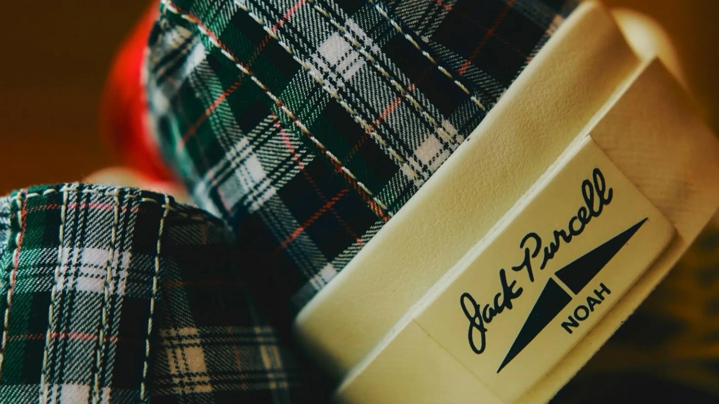 Close-up of green and white plaid fabric with a beige label reading "Jack Purcell NOAH.