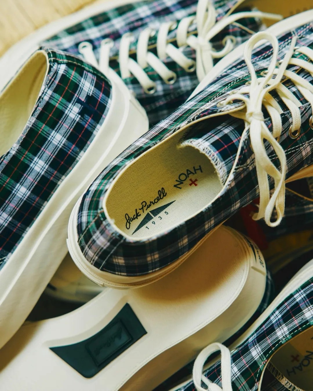Pair of plaid canvas sneakers with white laces and thick off-white rubber soles, branded Jack Purcell + Noah.