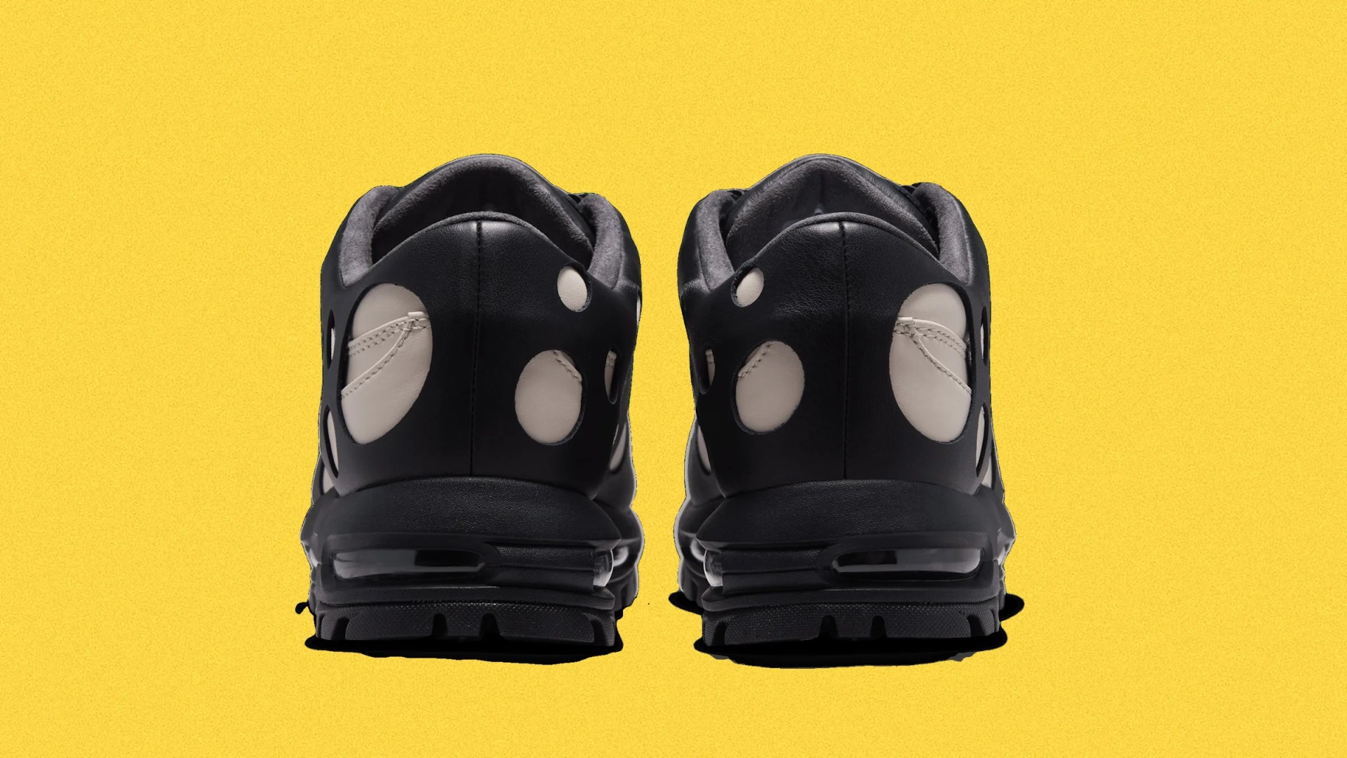 Pair of black sneakers with white circular cutouts on the heel against a yellow background.