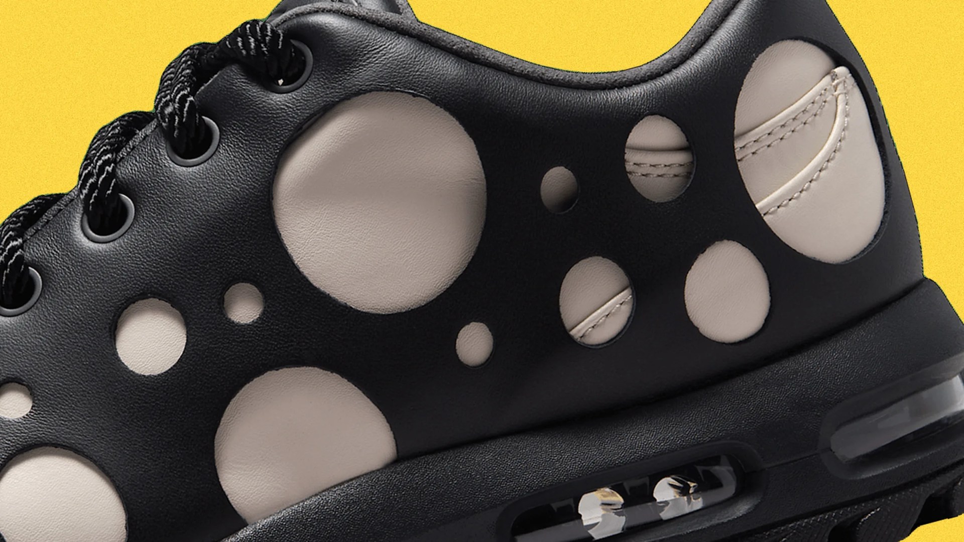 Close-up of black sneaker with large circular cutouts revealing beige leather underneath and visible air cushion in sole.