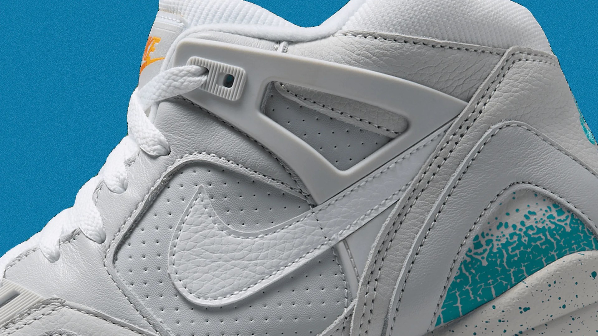 Close-up of white Nike sneaker with perforated leather, plastic lace holder, and teal speckled midsole detail.
