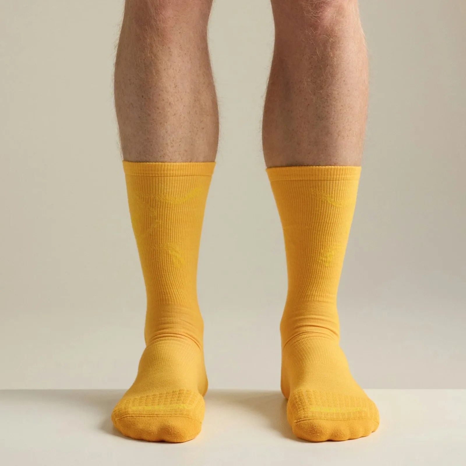Pair of bright yellow crew socks worn on legs against a neutral background.
