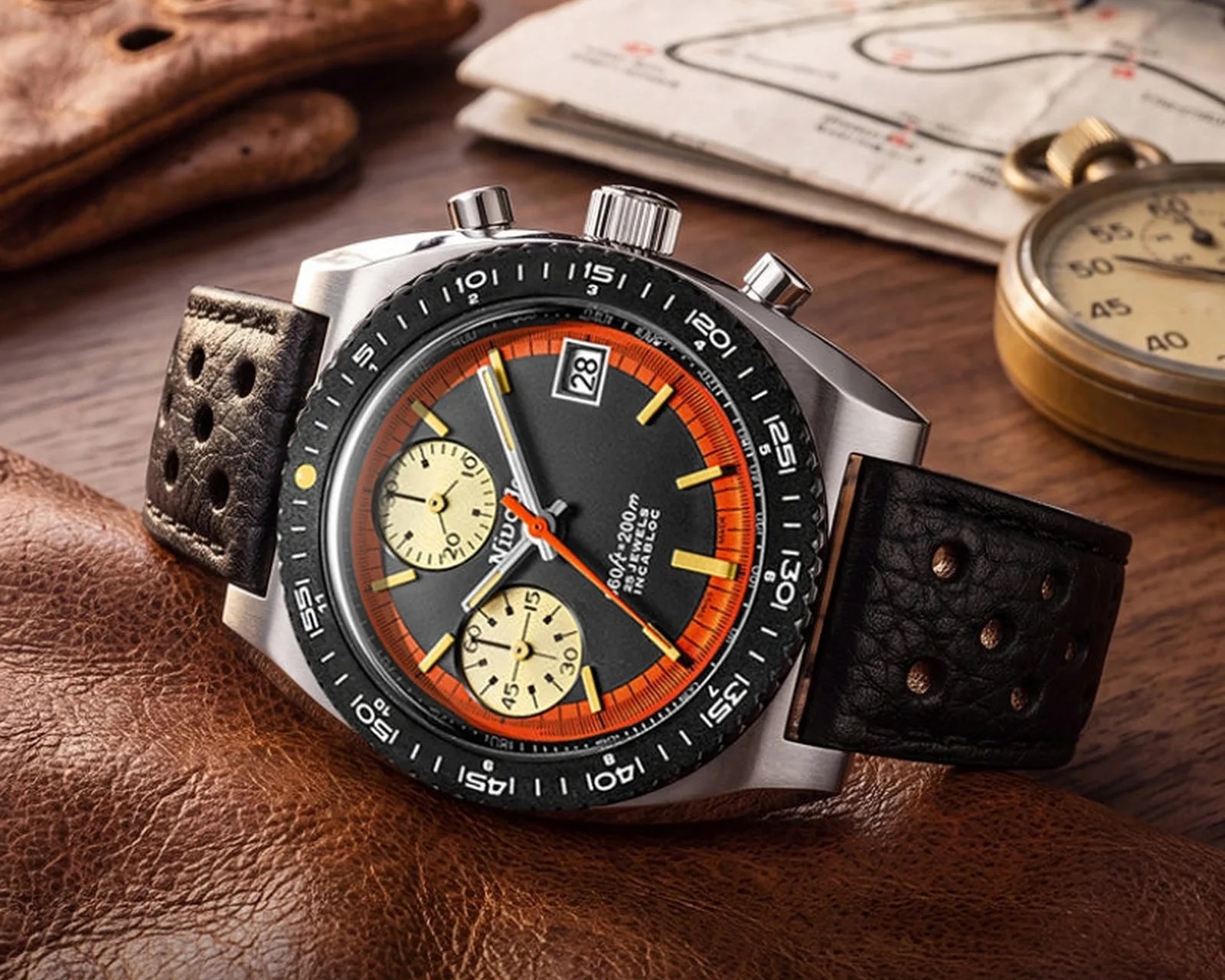 Chronograph wristwatch with black dial, orange ring, yellow markers, black perforated leather strap, and stainless steel case.