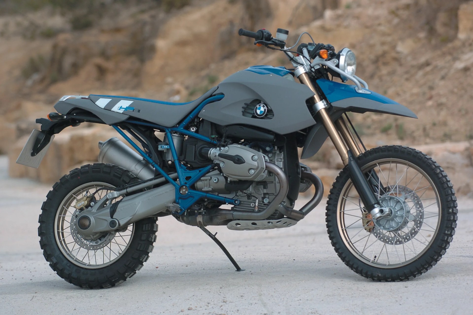 Blue and gray BMW off-road motorcycle with knobby tires parked on a dirt surface.