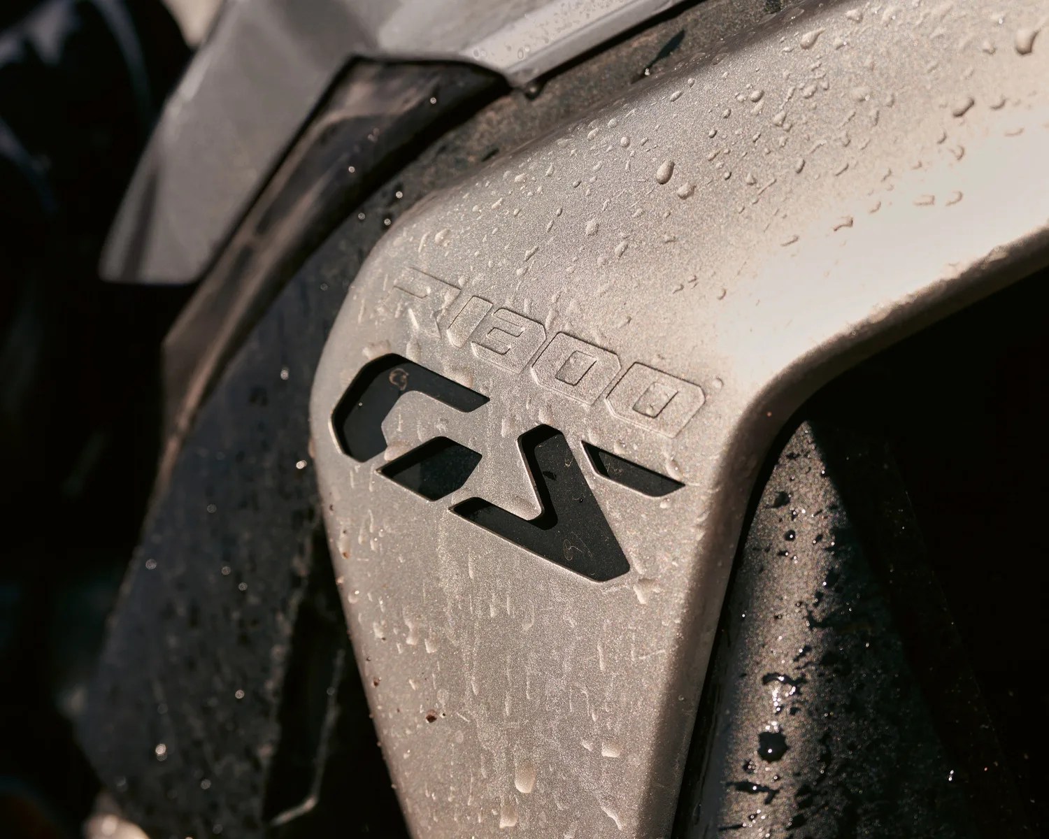 Close-up of a wet metallic surface with "R1200 GS" embossed on it, likely part of a motorcycle.