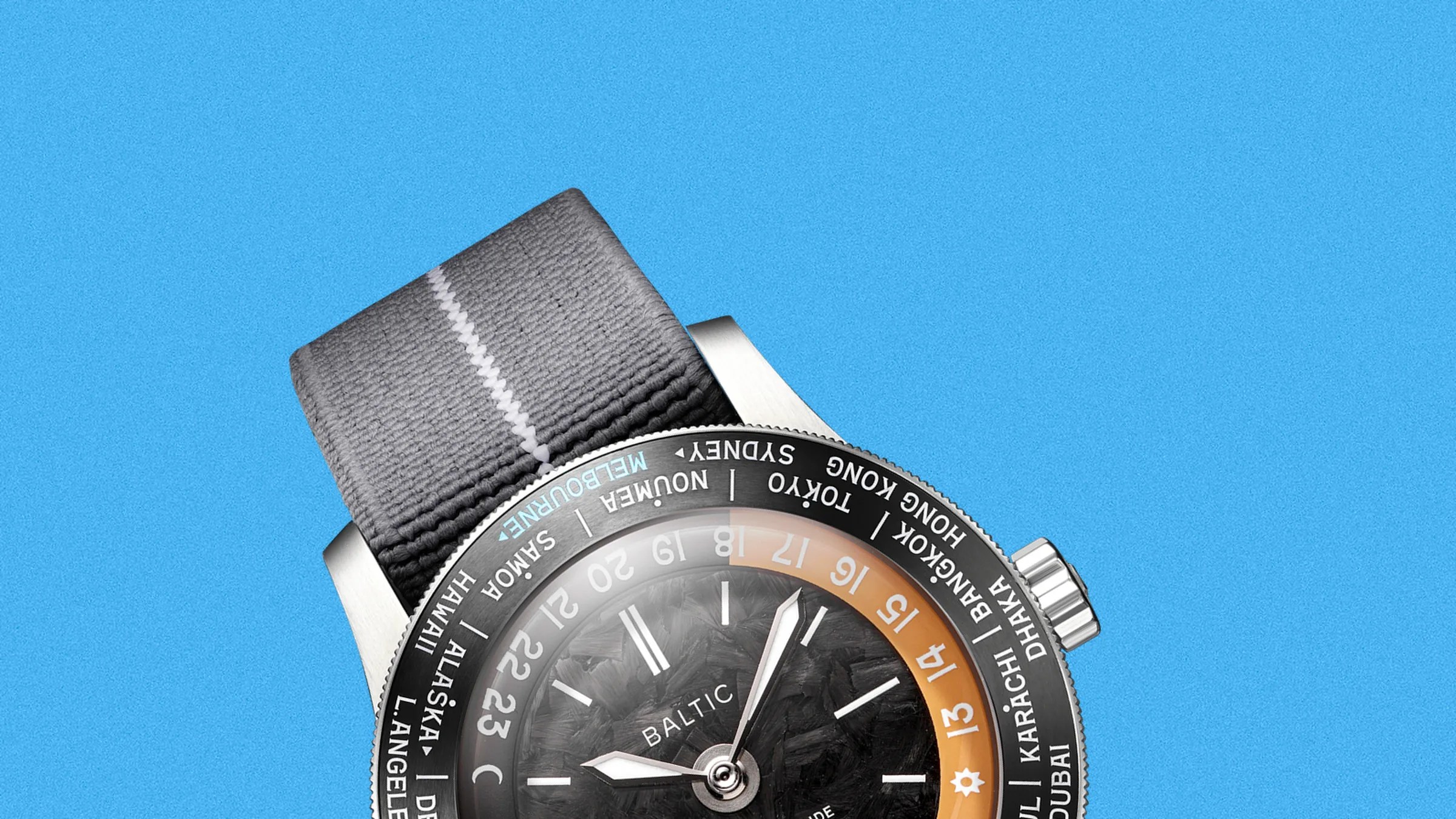 Close-up of a Baltic wristwatch with a black textured dial, orange 24-hour ring, and gray fabric strap on a blue background.