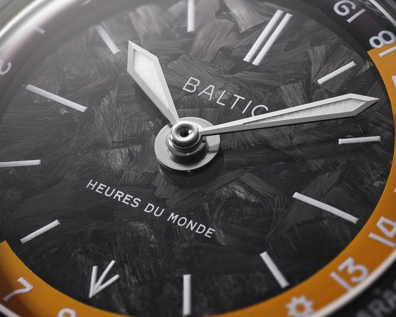 Close-up of a Baltic watch dial with textured black face, white hour markers, and silver hands, featuring "HEURES DU MONDE" text.