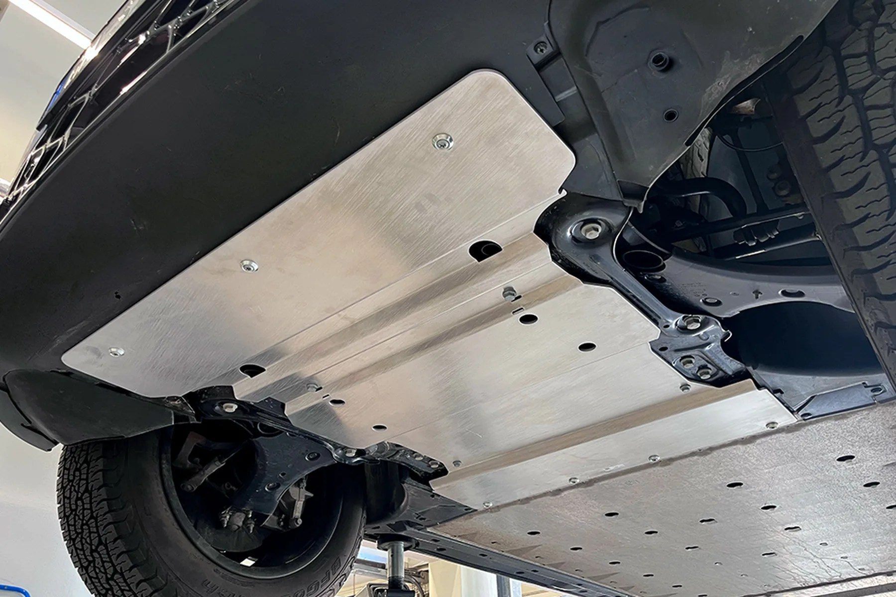 Aluminum skid plate installed under a vehicle, covering the front suspension and frame area.
