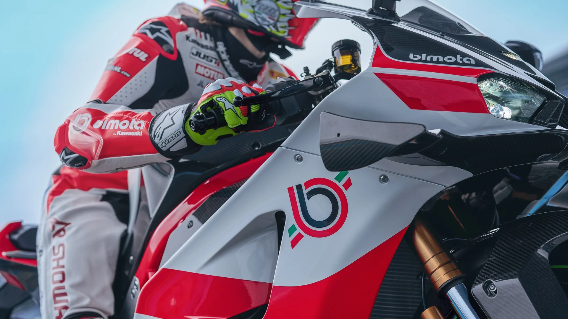 Close-up of a red, white, and black Bimota motorcycle with a rider in matching gear gripping the handlebar.
