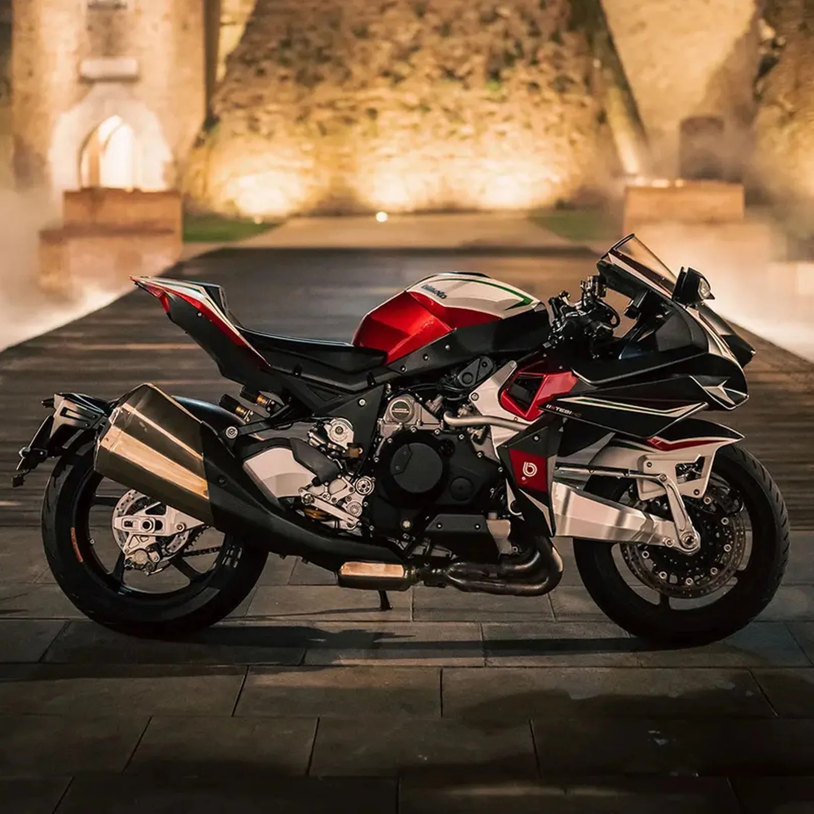 Black and red sport motorcycle parked on a stone pavement with illuminated stone walls in the background.