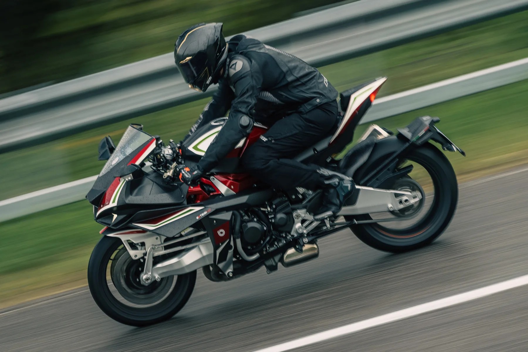 Sport motorcycle with black, red, and white fairings ridden by a person in black gear on a road.