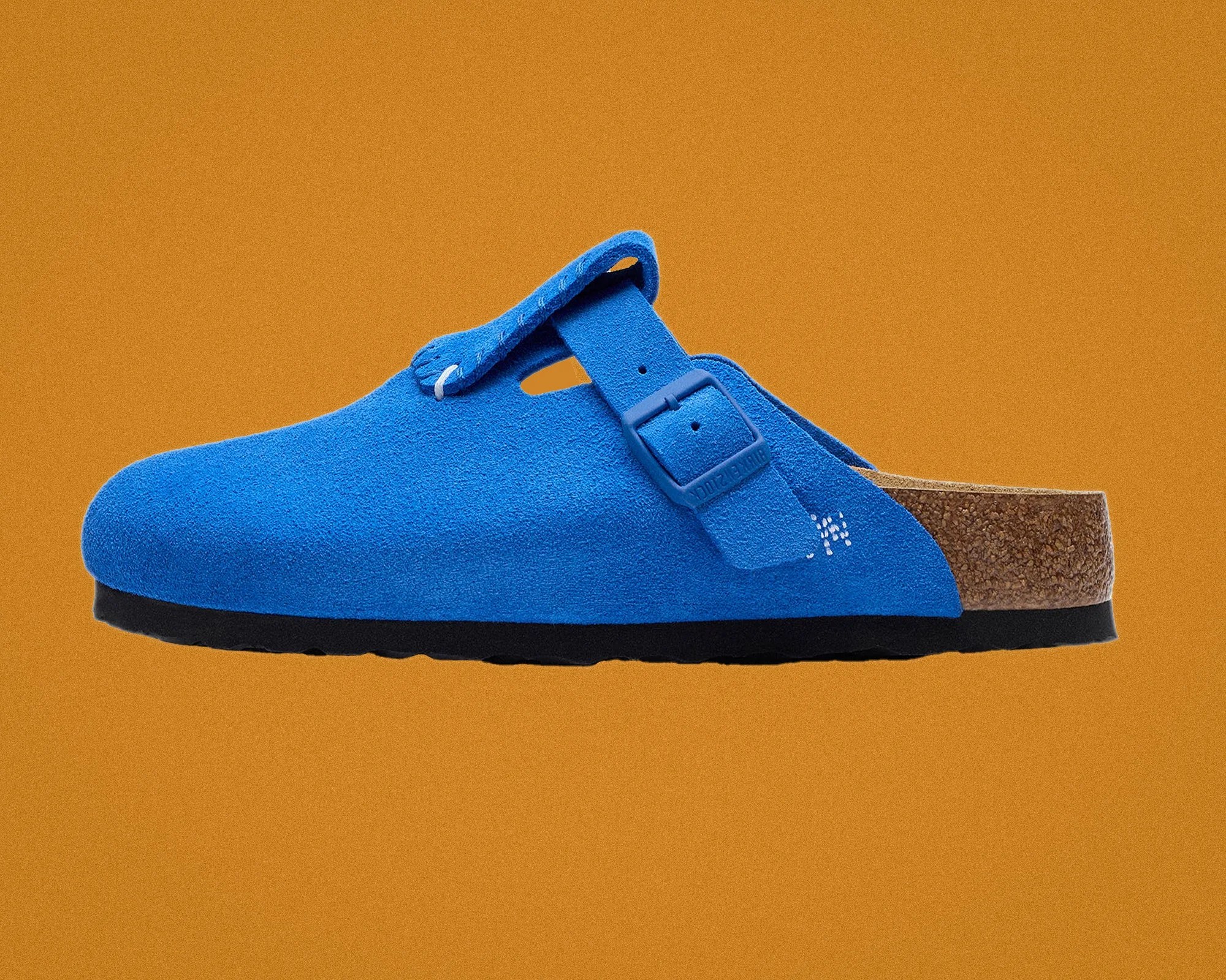 Blue suede clog with adjustable strap and cork footbed on an orange background.