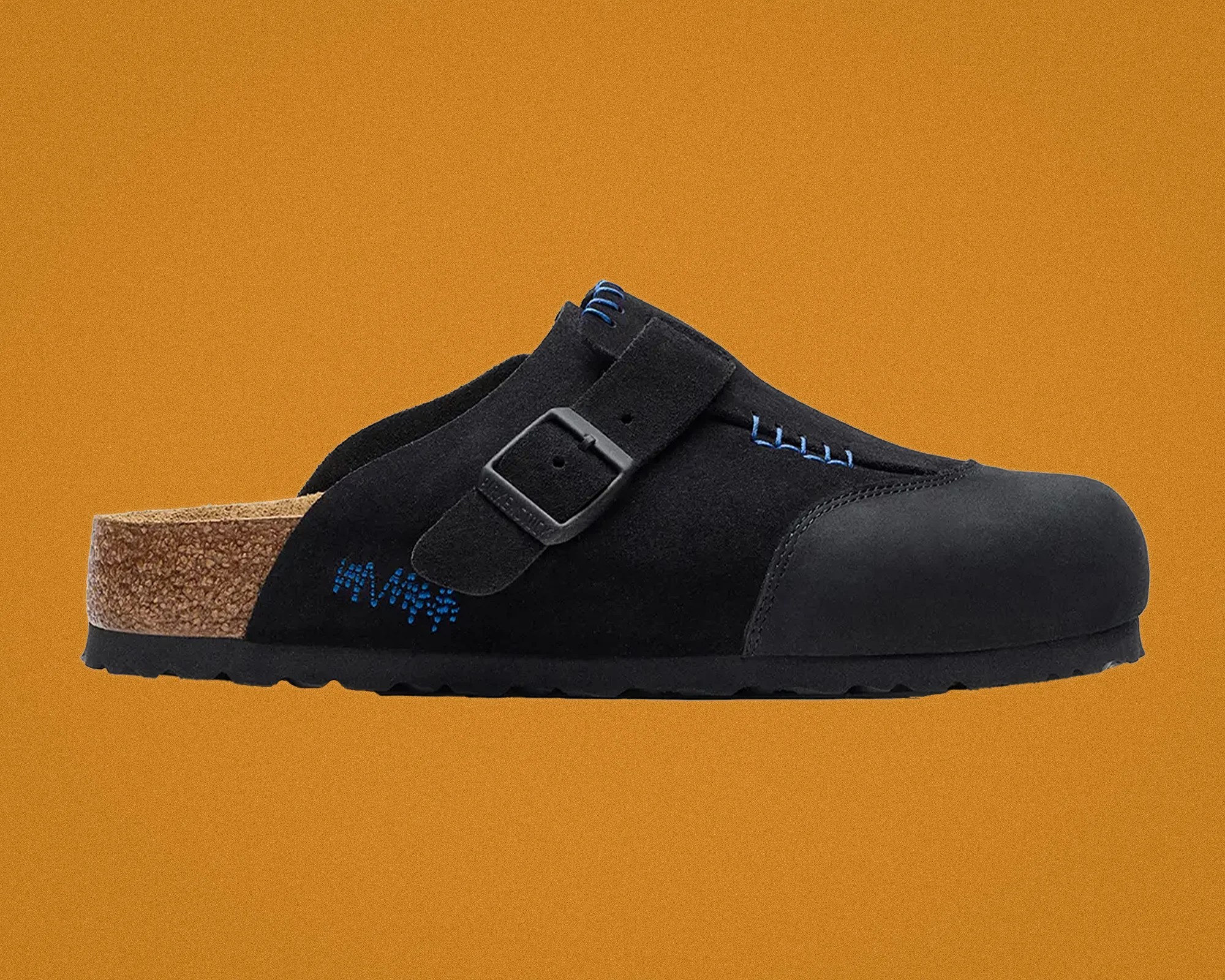 Black suede slip-on clog with blue stitching, adjustable buckle strap, and cork footbed on an orange background.