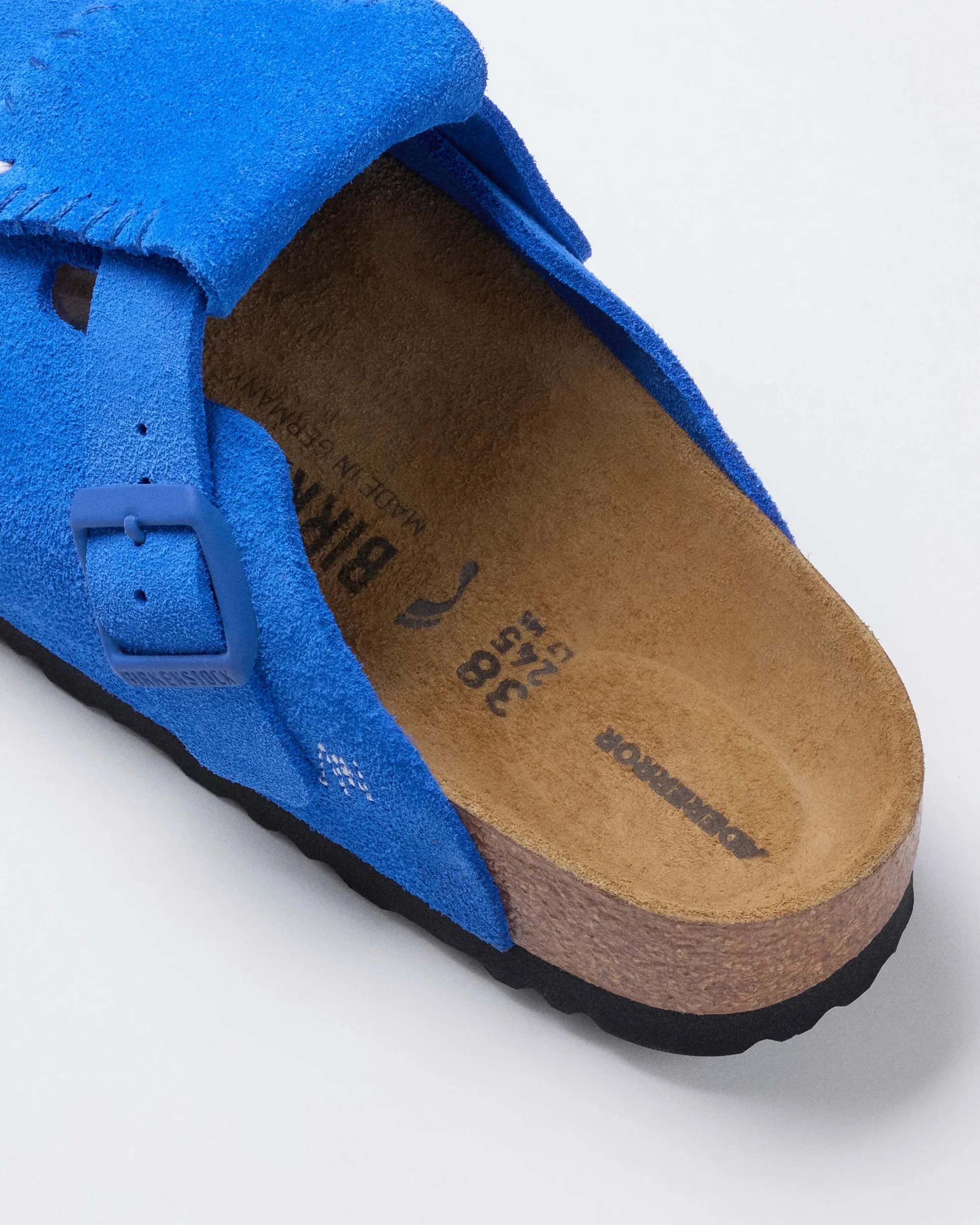 Blue suede Birkenstock sandal with cork footbed and black sole on a white background.
