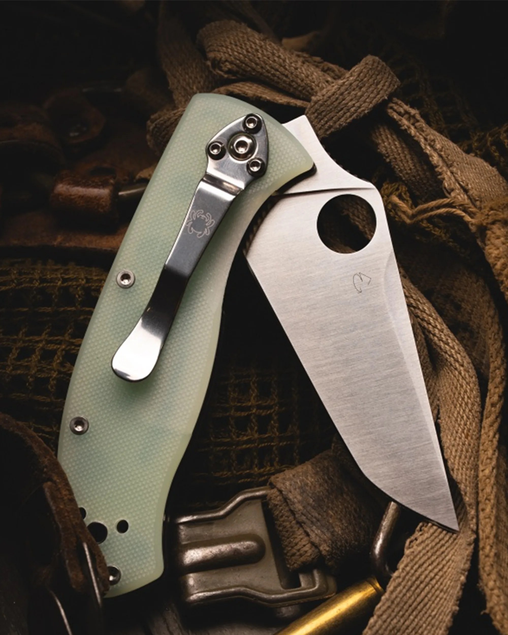 Folding knife with a light green textured handle and a stainless steel blade featuring a circular hole near the base.