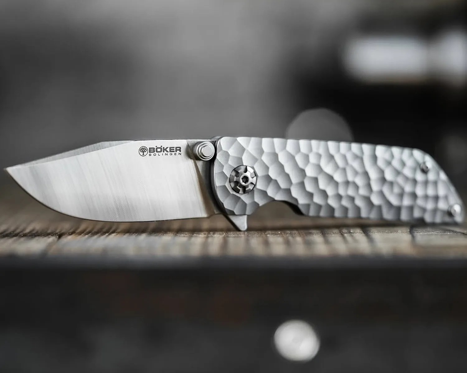 Silver Böker folding knife with textured handle resting on a wooden surface.