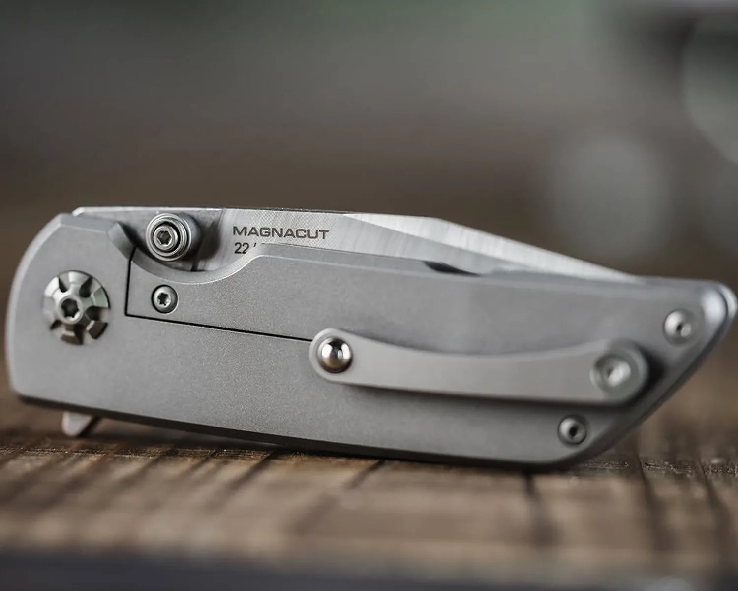 Closed gray folding knife with a partially visible blade labeled "MAGNACUT 22" on a wooden surface.