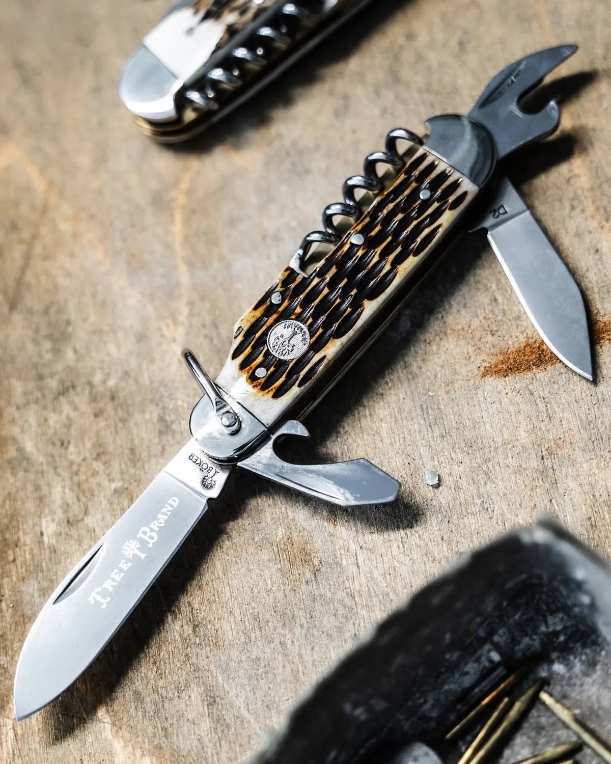 Multi-tool pocket knife with a textured brown handle, corkscrew, and several open blades on a wooden surface.